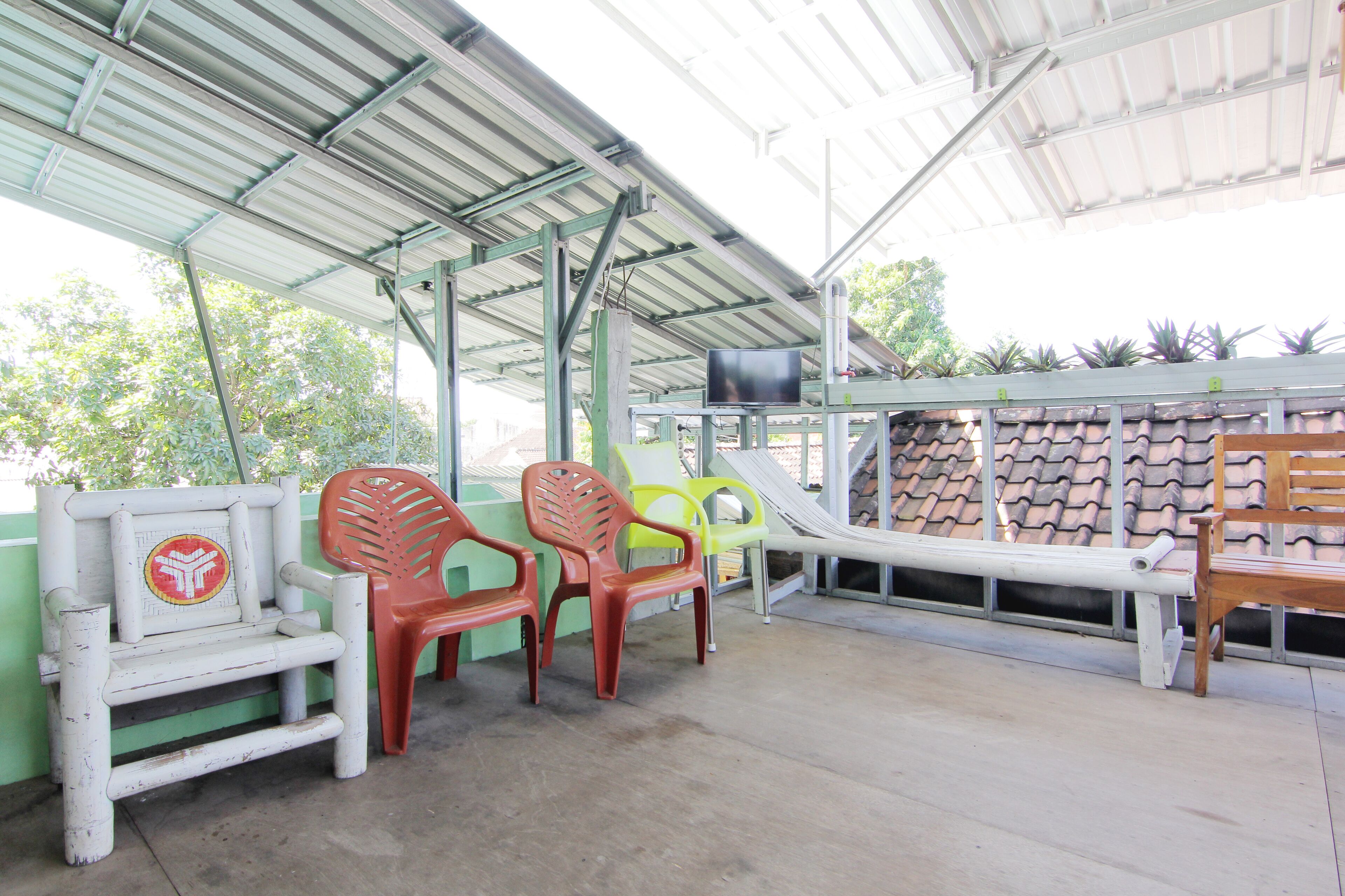 A covered outdoor seating area with plastic chairs and a bench, a television mounted on the wall, and a slide.