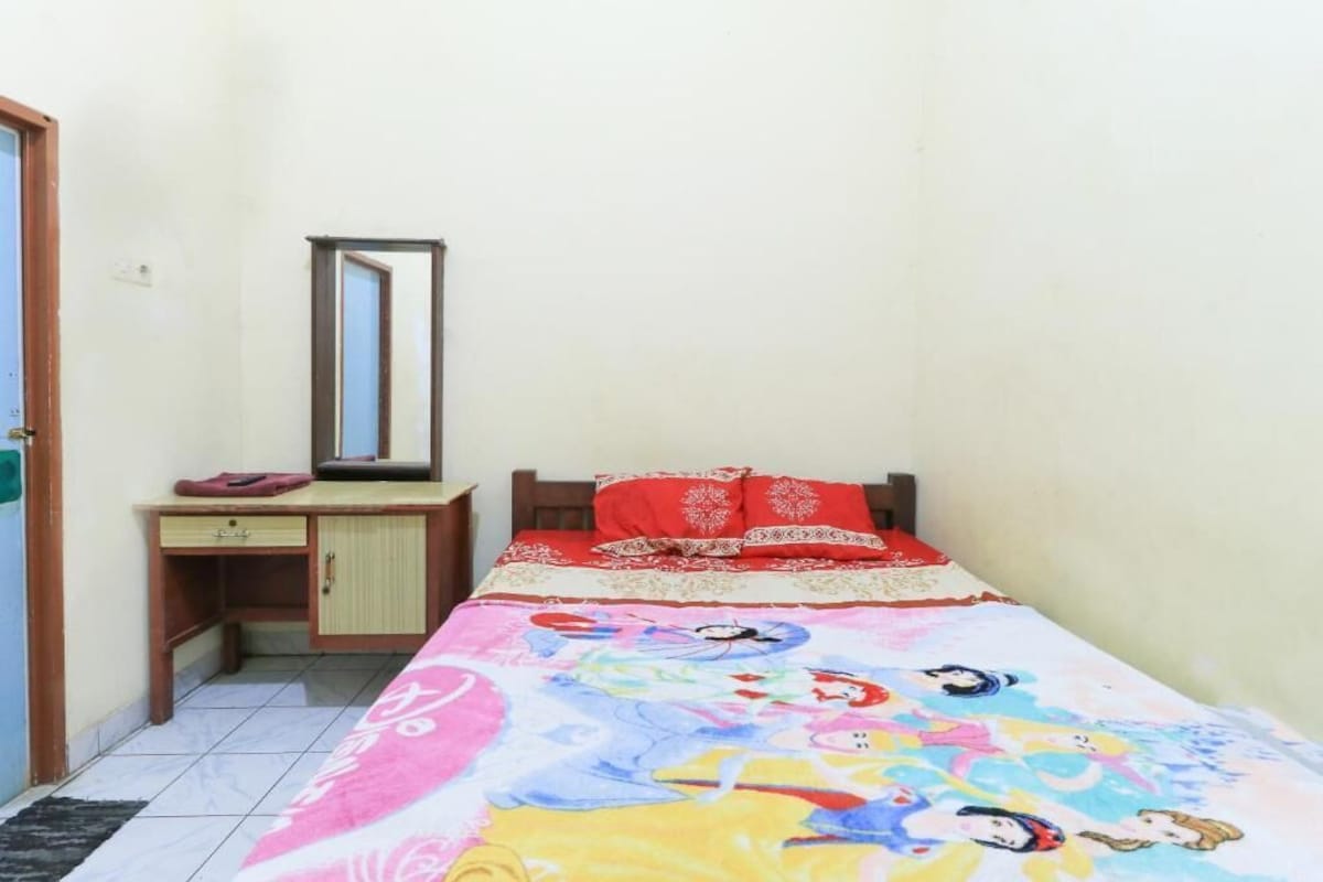 A small bedroom with a bed, a desk, and a mirror.