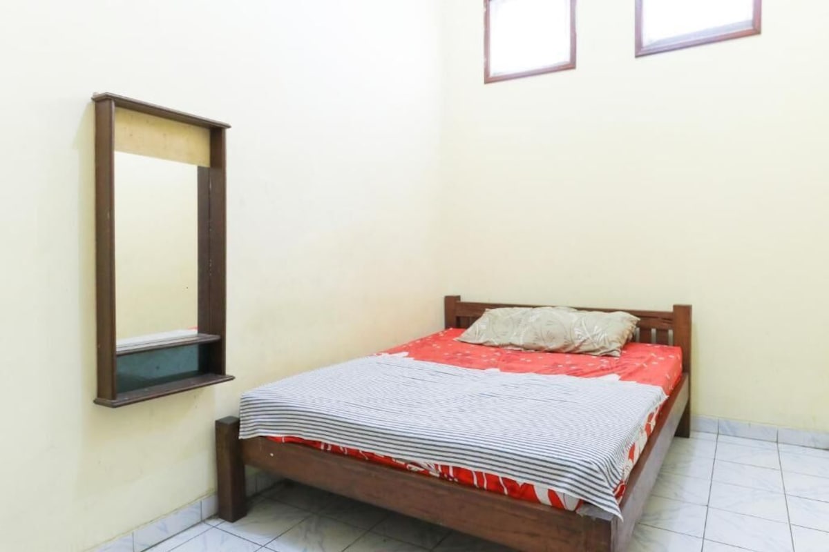 A single bed with a wooden frame, a red and white bedspread, and a wooden headboard.