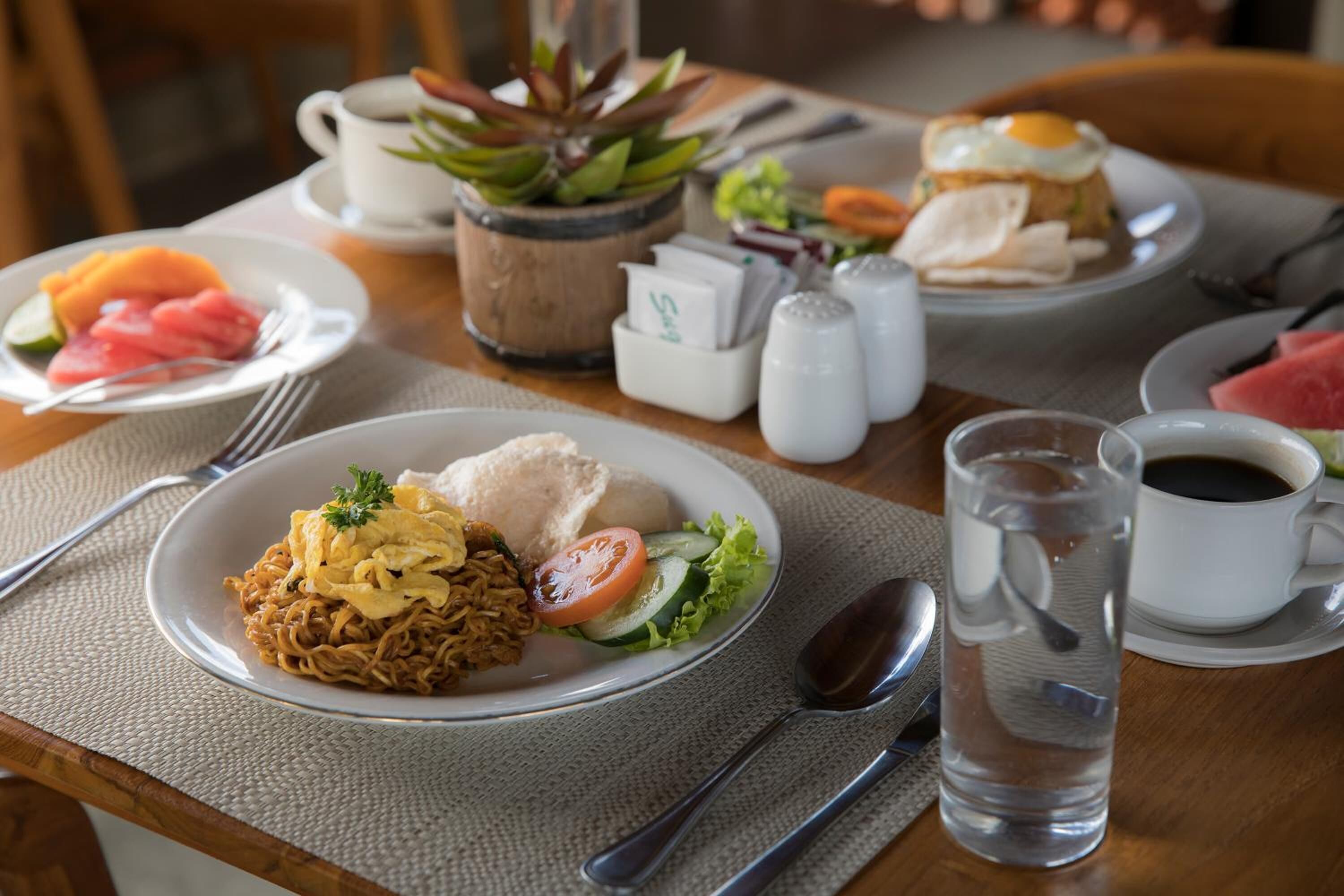 A table with plates of food, a water pitcher, salt and pepper shakers, and a cup of coffee.