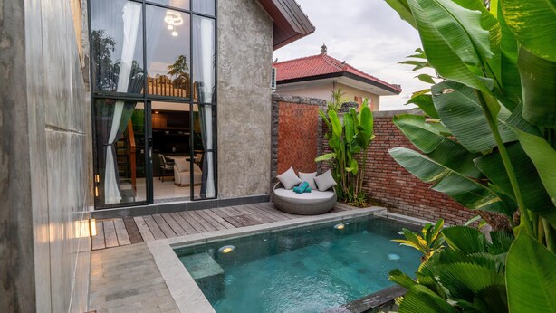 Una casa moderna con piscina, terraza de madera y exuberante vegetación.