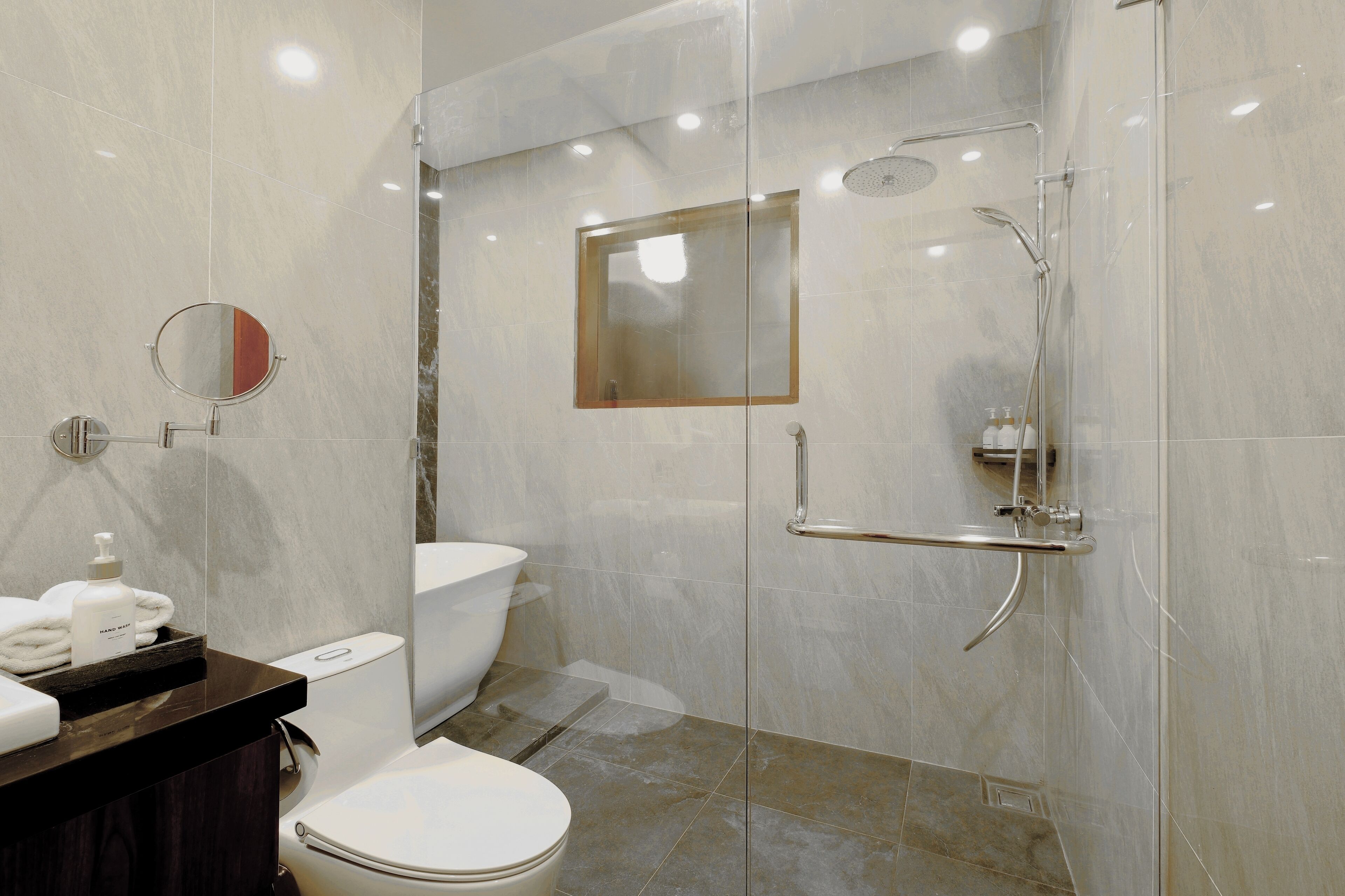 Een moderne badkamer met een douche in een glazen cabine, toilet en een wastafel met spiegel en toiletartikelen.