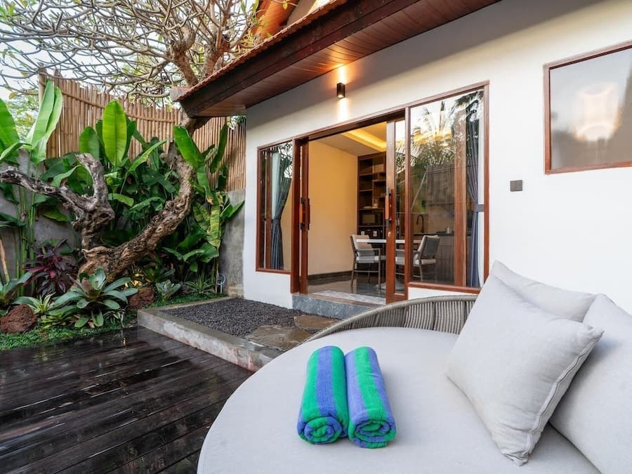 Una habitación con terraza de madera, un sofá con cojín y un par de toallas enrolladas.