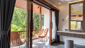 Una habitación moderna con balcón, una silla de madera, un otoman redondo y un espejo grande.