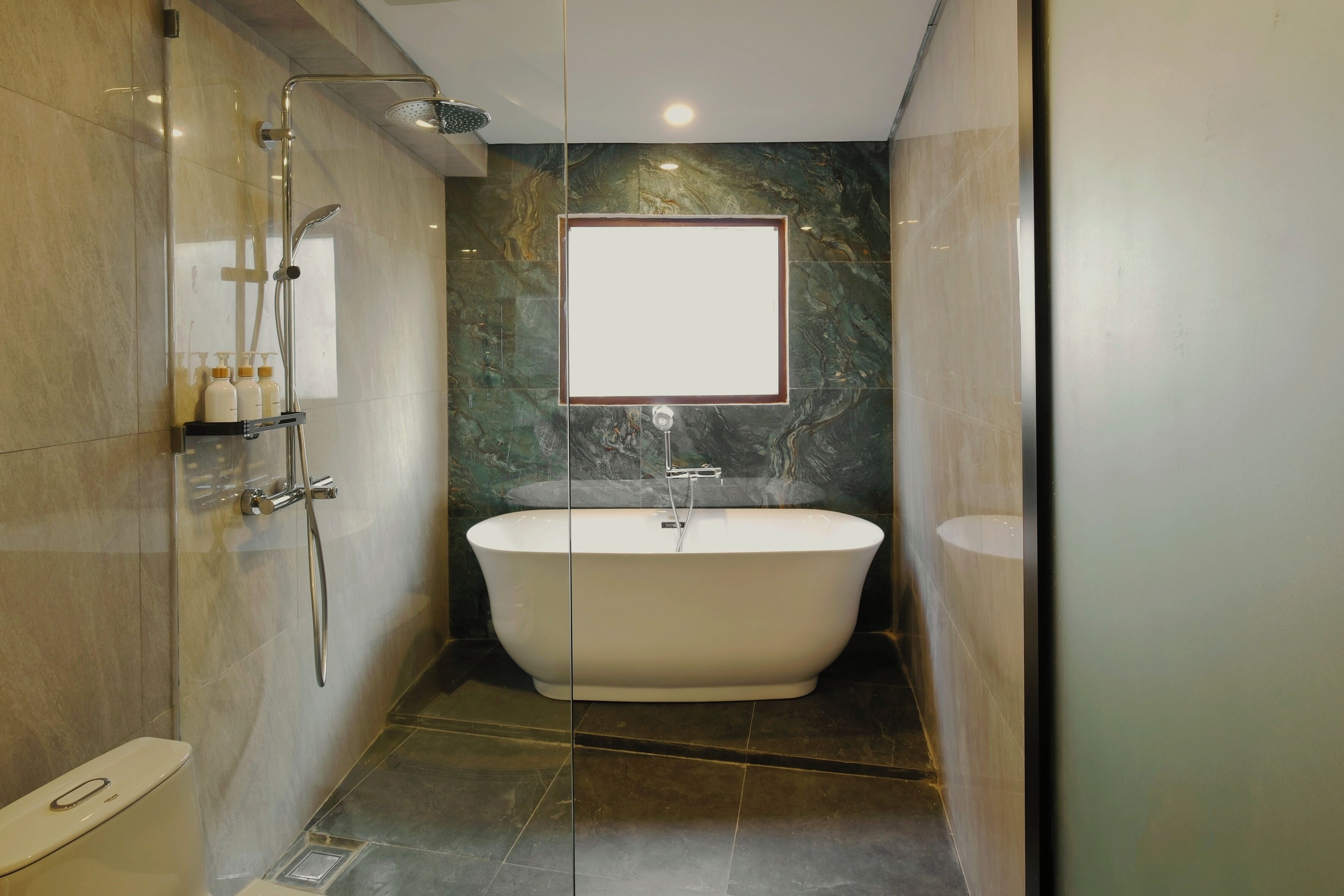 Un baño moderno con una bañera independiente, cabina de ducha con mampara de vidrio y pared de mármol.