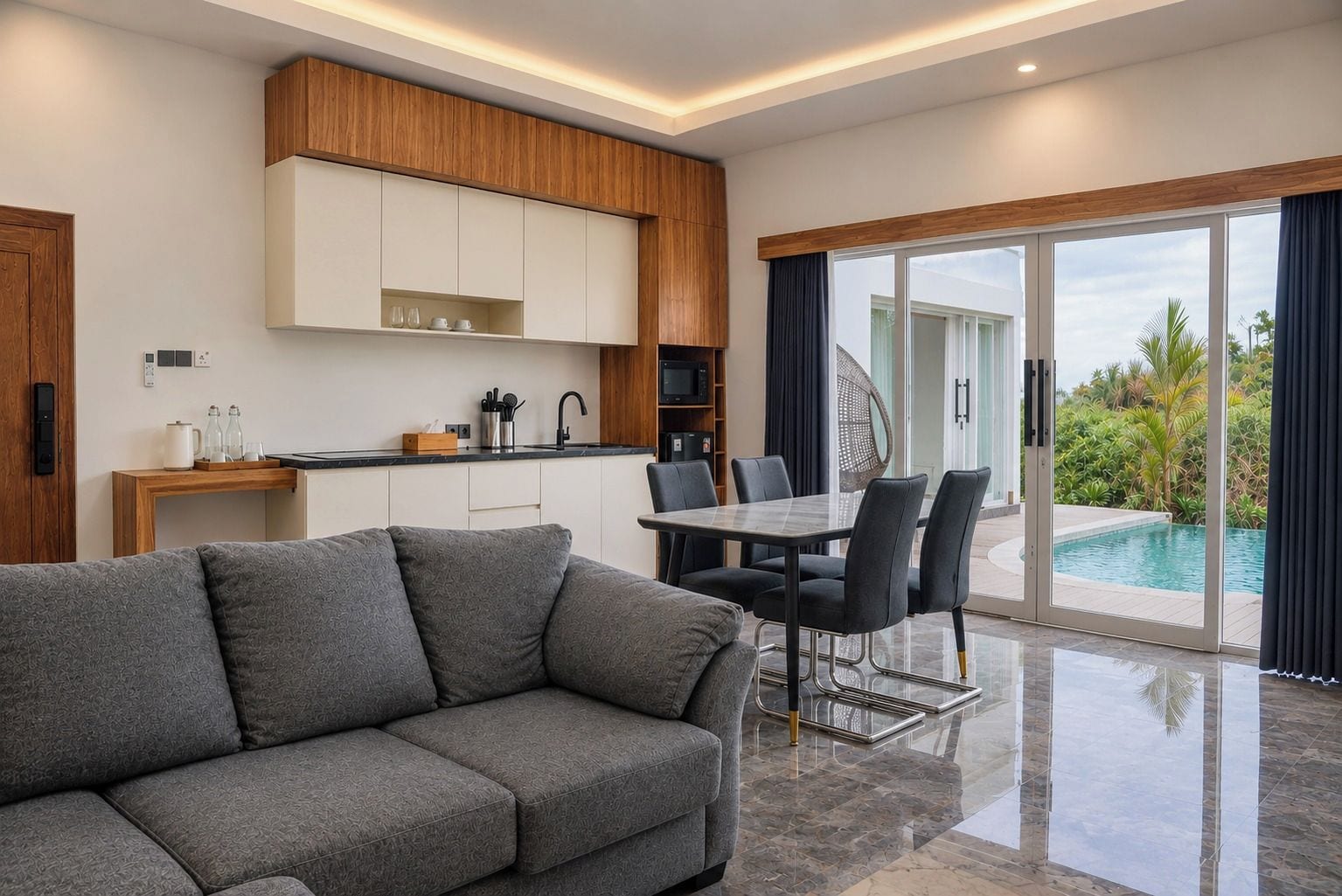 Una sala de estar moderna con un sofá gris, un comedor con mesa y sillas, una cocina con armarios de madera y una puerta de vidrio que da a una piscina.