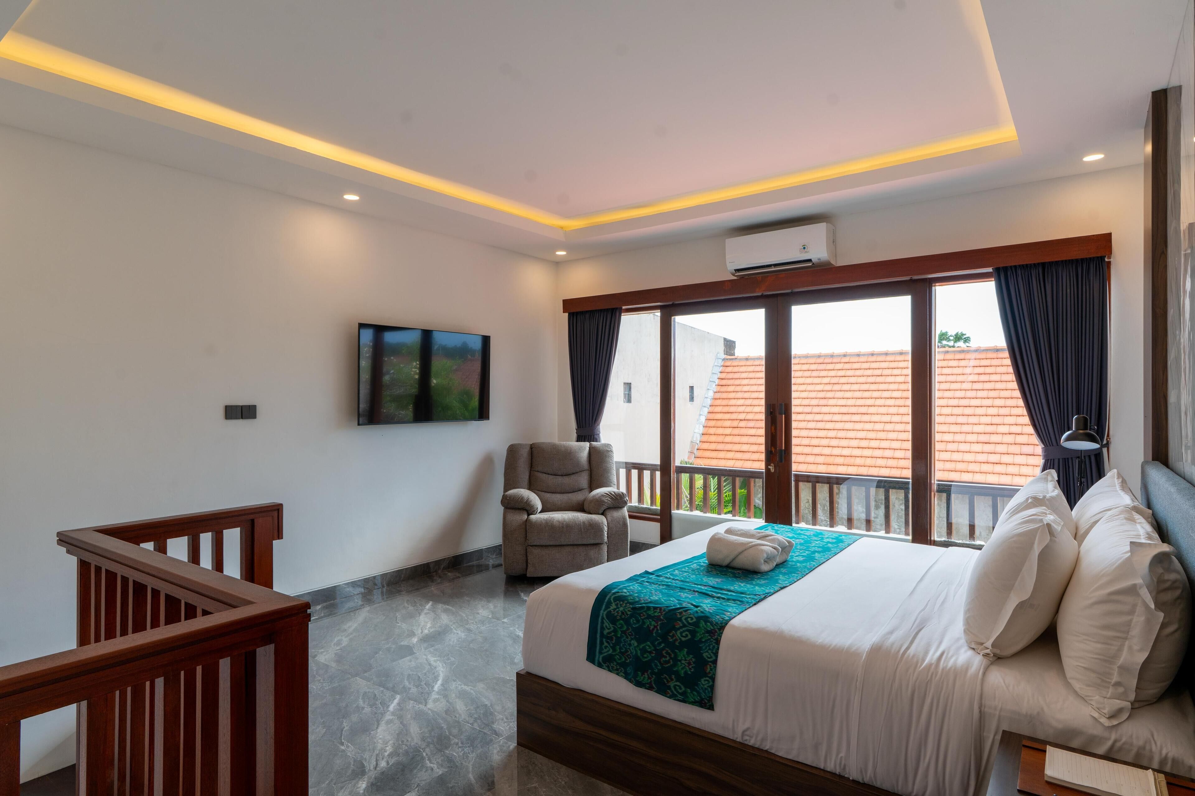 A hotel room with a bed, a chair, a TV, and a balcony with a view of buildings.