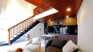 Una sala de estar moderna con un sofá, una mesa de centro con fruta, una escalera y una zona de cocina.