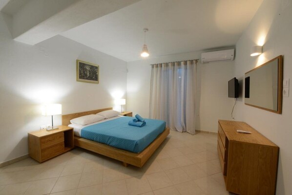 A bedroom with a wooden bed, two bedside tables with lamps, a TV, a mirror, and a window with curtains. - Wild View Mykonos (Mykonos)