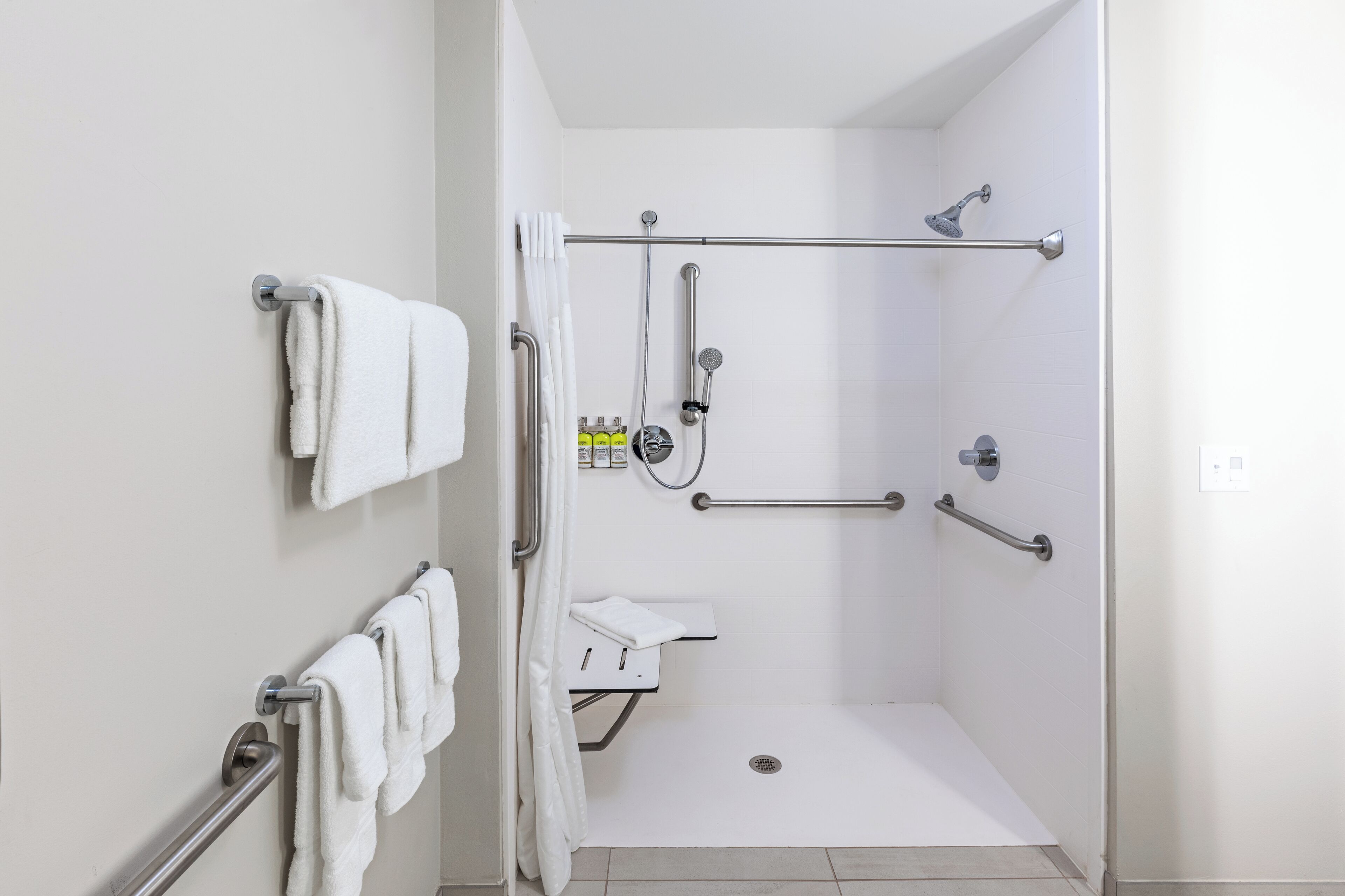 A modern bathroom with a walk-in shower, grab bars, and a white tiled floor.