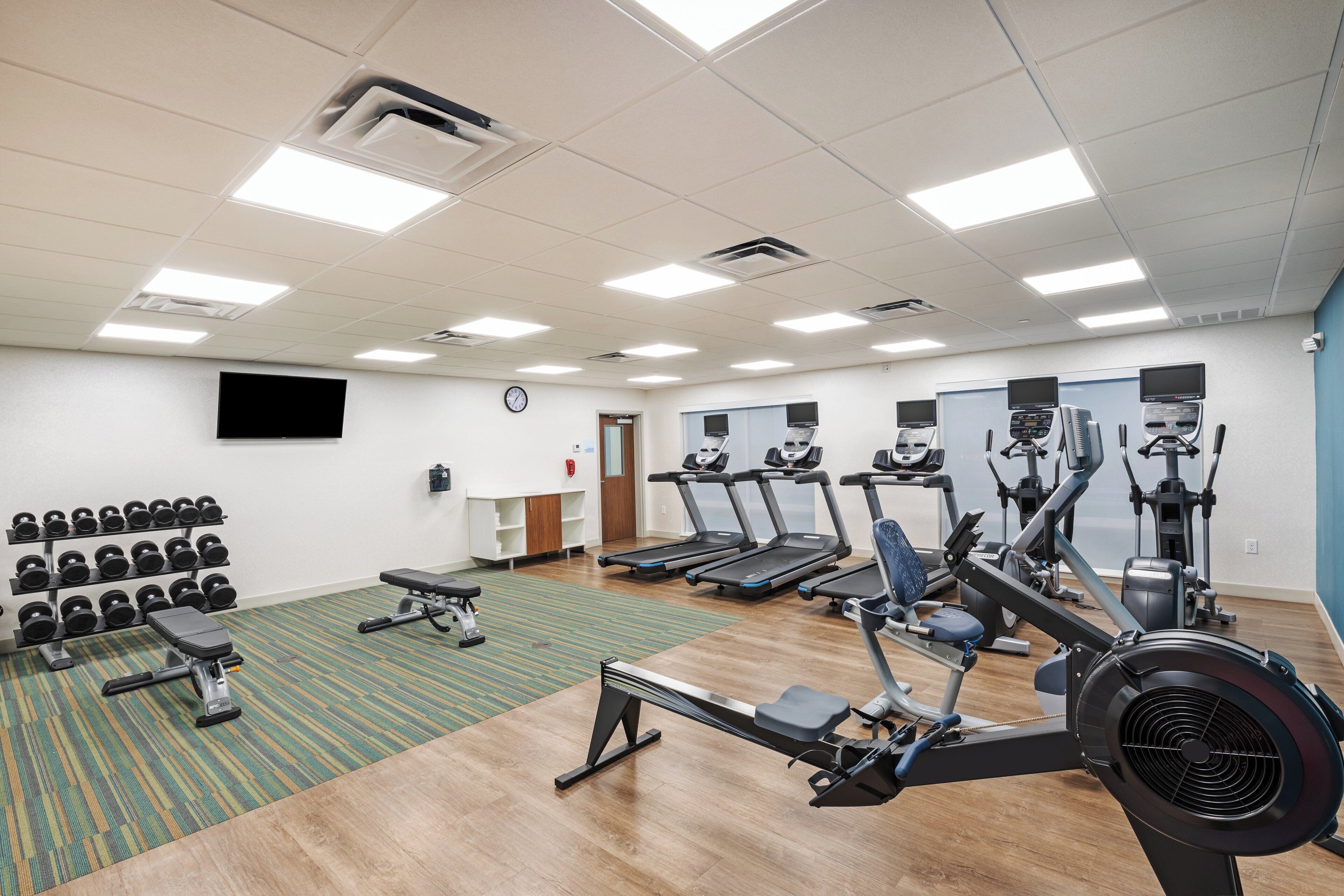 A gym with treadmills, elliptical machines, and a rack of dumbbells.