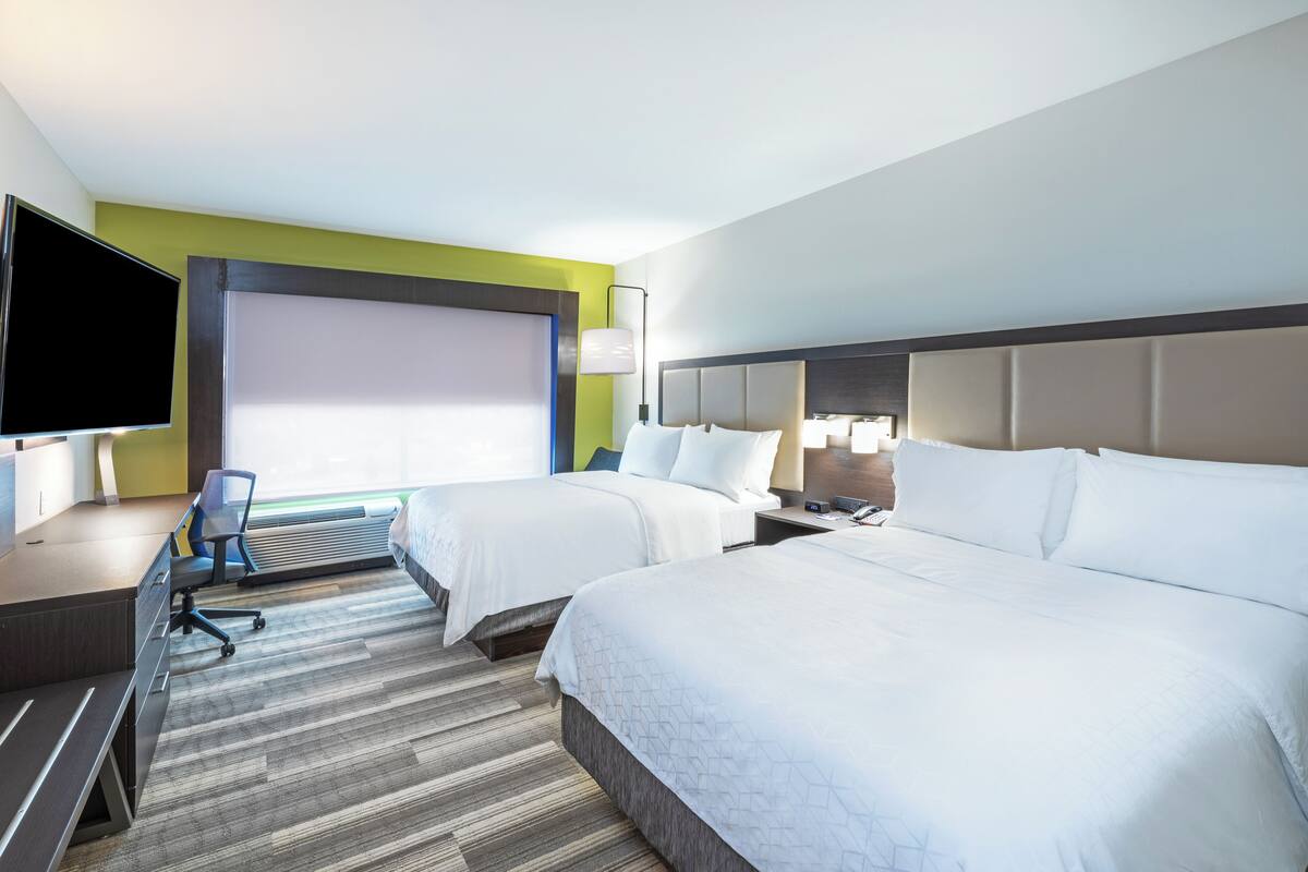 A hotel room with two beds, a desk, a chair, a flat-screen TV, and a large window.