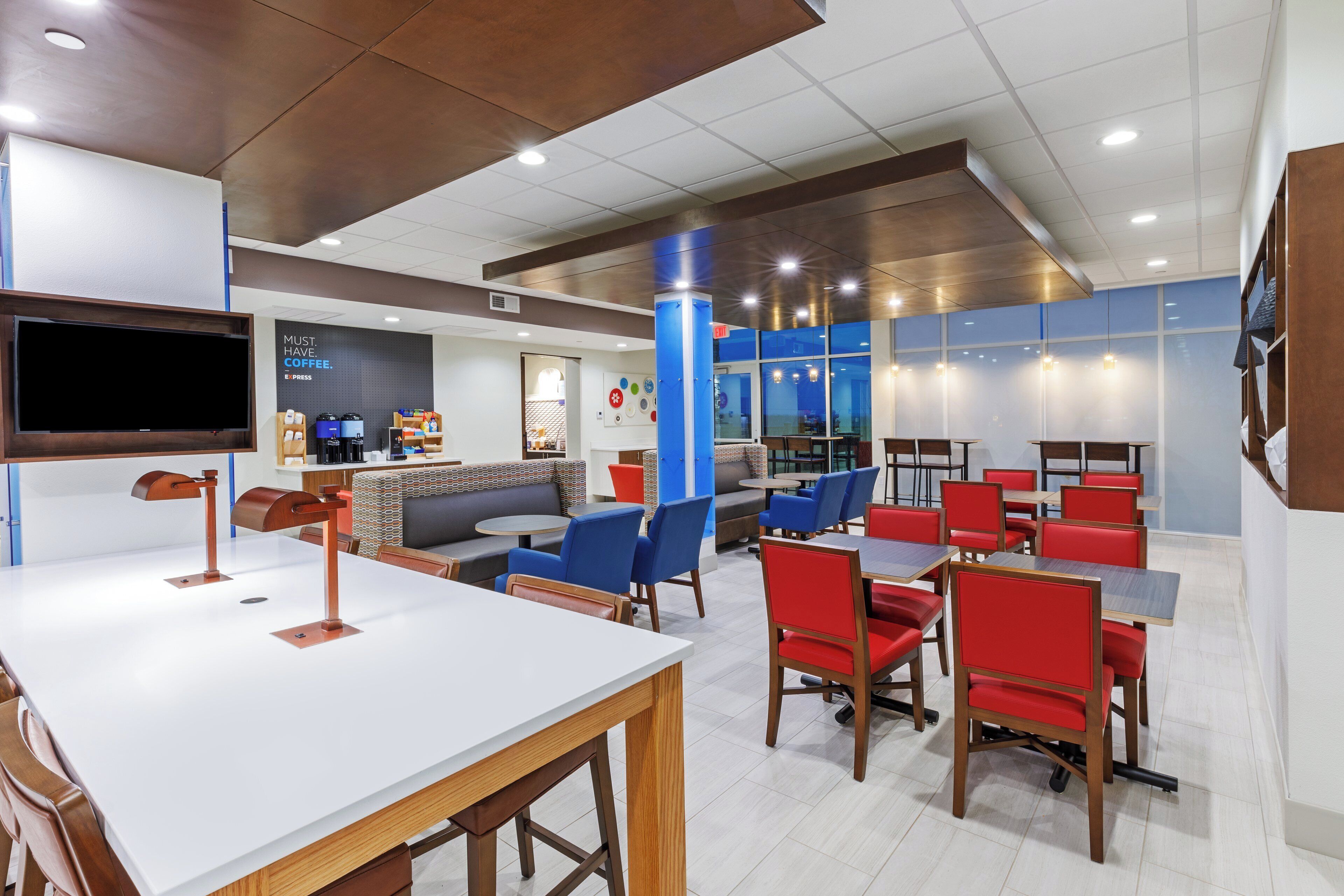 A modern cafe with a flat-screen TV, seating areas, and a coffee machine.