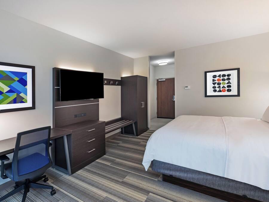 A hotel room with a bed, desk, chair, TV, wardrobe, and artwork on the walls.