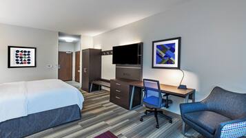 A hotel room with a bed, desk, chair, TV, and artwork.