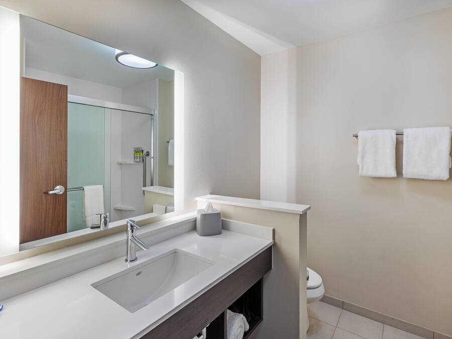 A modern bathroom with a large mirror, a sink, a towel rack, and a toilet.