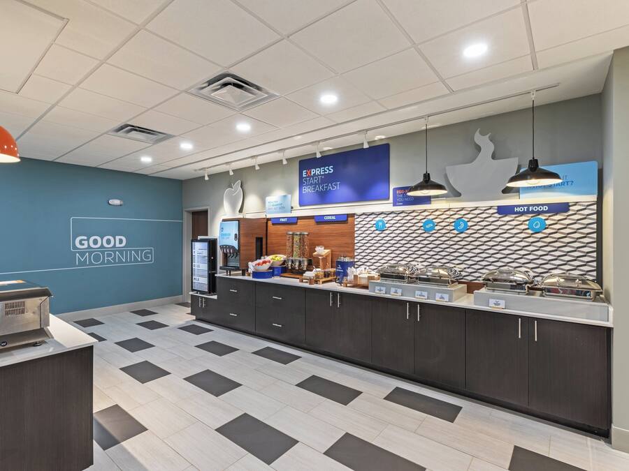 A breakfast area with a counter displaying various food options, a sign for Express Start Breakfast, and a wall with a 'Good Morning' message.