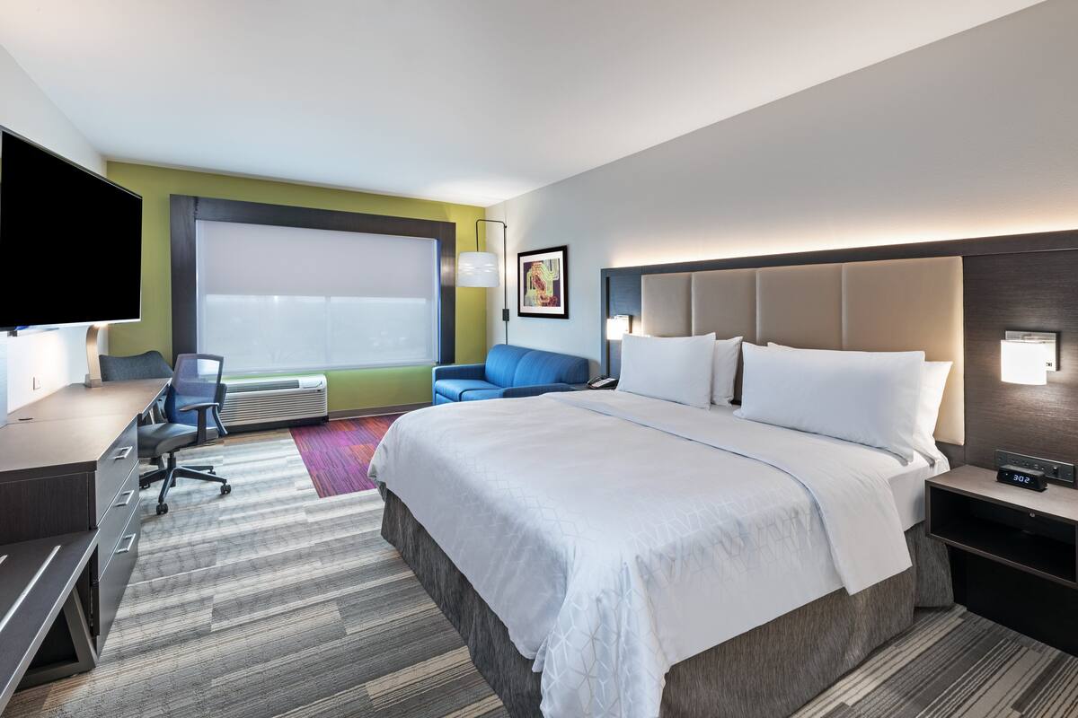 A modern hotel room with a large bed, a desk, a chair, and a TV.