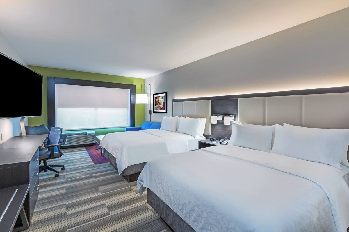 A hotel room with two beds, a desk, a chair, a TV, and a large window.