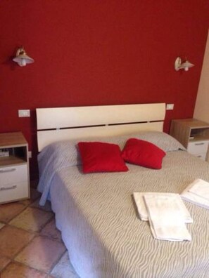 Ein Schlafzimmer mit einem Bett, zwei roten Kissen, einem weißen Kopfteil und zwei Nachttischen mit Lampen.