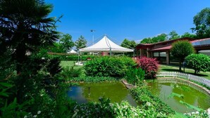 Un jardin avec un étang, une tente blanche et un bâtiment avec un toit rouge.
