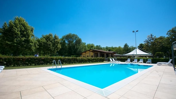 Une piscine rectangulaire avec une terrasse carrelée, entourée de chaises longues et d’un belvédère.