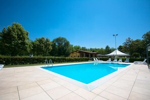 Une piscine rectangulaire avec une terrasse carrelée, entourée de chaises longues et d’un belvédère.