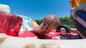 Une structure gonflable de grande taille, à la forme incurvée, et aux couleurs rouge et blanche, qui pourrait servir de toboggan ou d’aire de jeux.