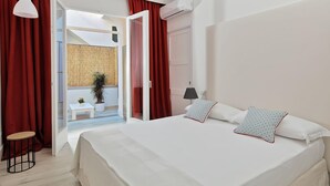 A hotel room with a large bed, red curtains, a small table, a chair, and an air conditioning unit. - Fuorlovado 40 (Capri)