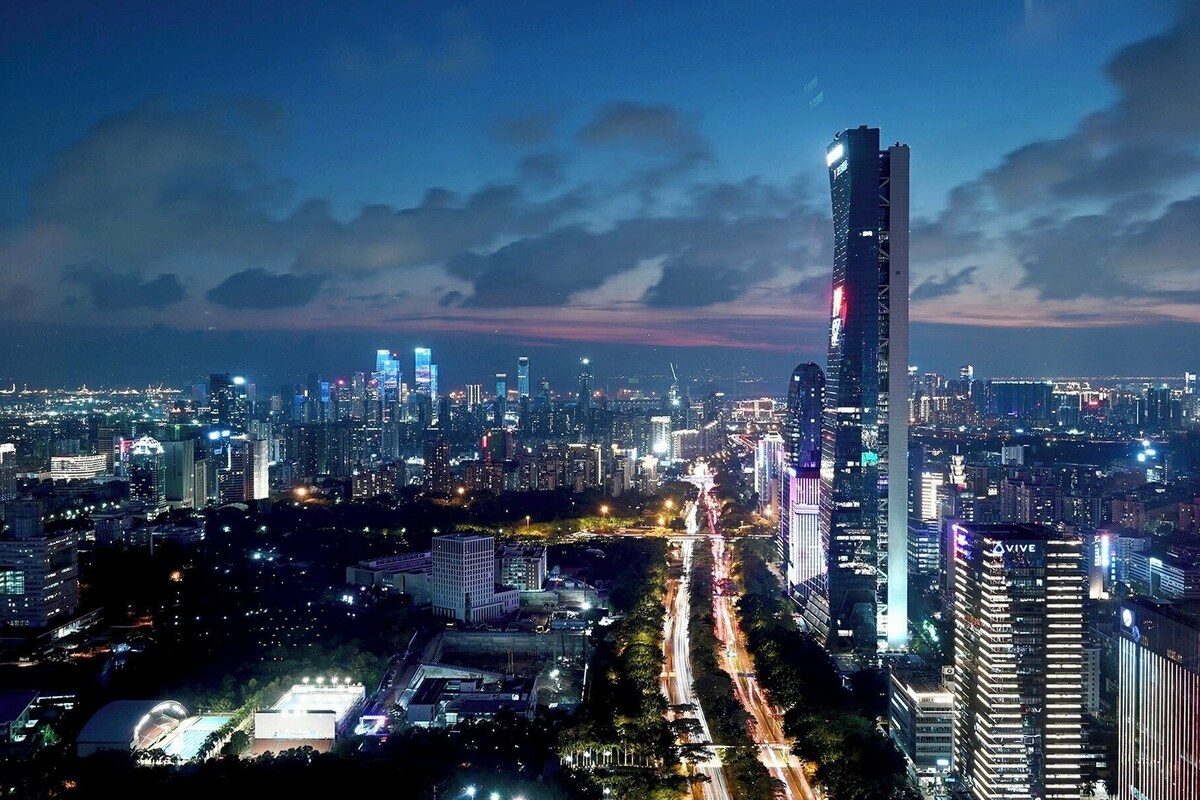 A nighttime cityscape with a prominent skyscraper, illuminated buildings, and a busy road.