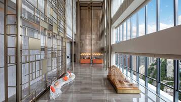 A modern hotel lobby with a reception desk, seating area, and large windows offering city views.