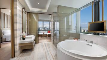 A modern bathroom with a large bathtub, a vanity with a mirror, and a view of the city through large windows.