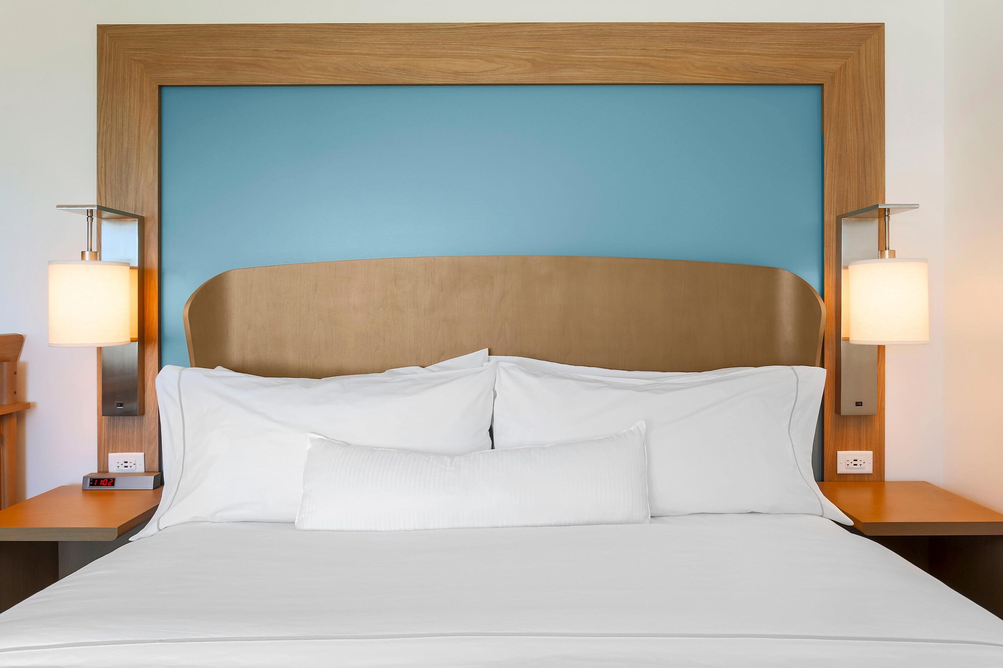 A neatly made bed with white linens, a wooden headboard, and two bedside lamps.