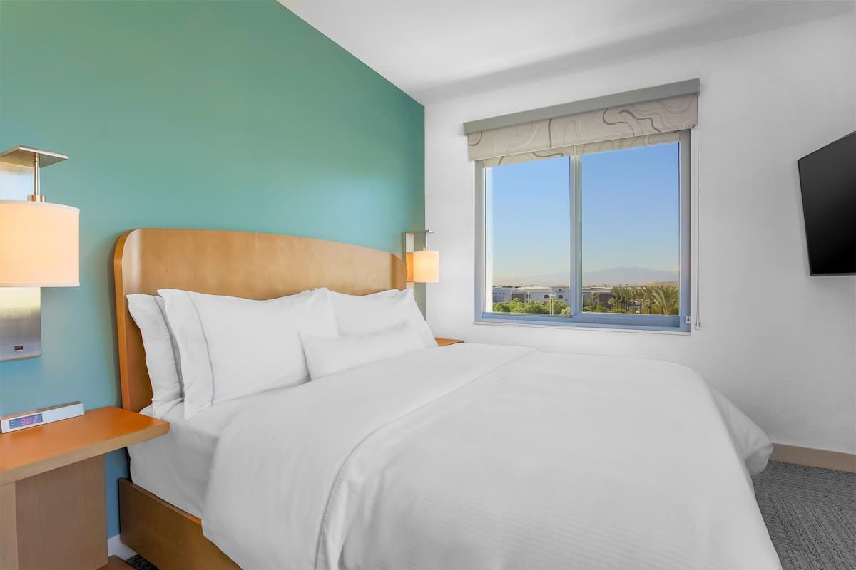 Une chambre d’hôtel avec un lit, une table de chevet avec une lampe, une télévision et une fenêtre donnant sur des immeubles.