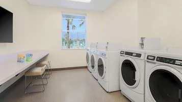 A laundry room with a white countertop, two bar stools, and a row of front-loading washing machines.