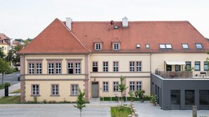 A two-story building with a red-tiled roof, multiple windows, and a small balcony on the upper floor.