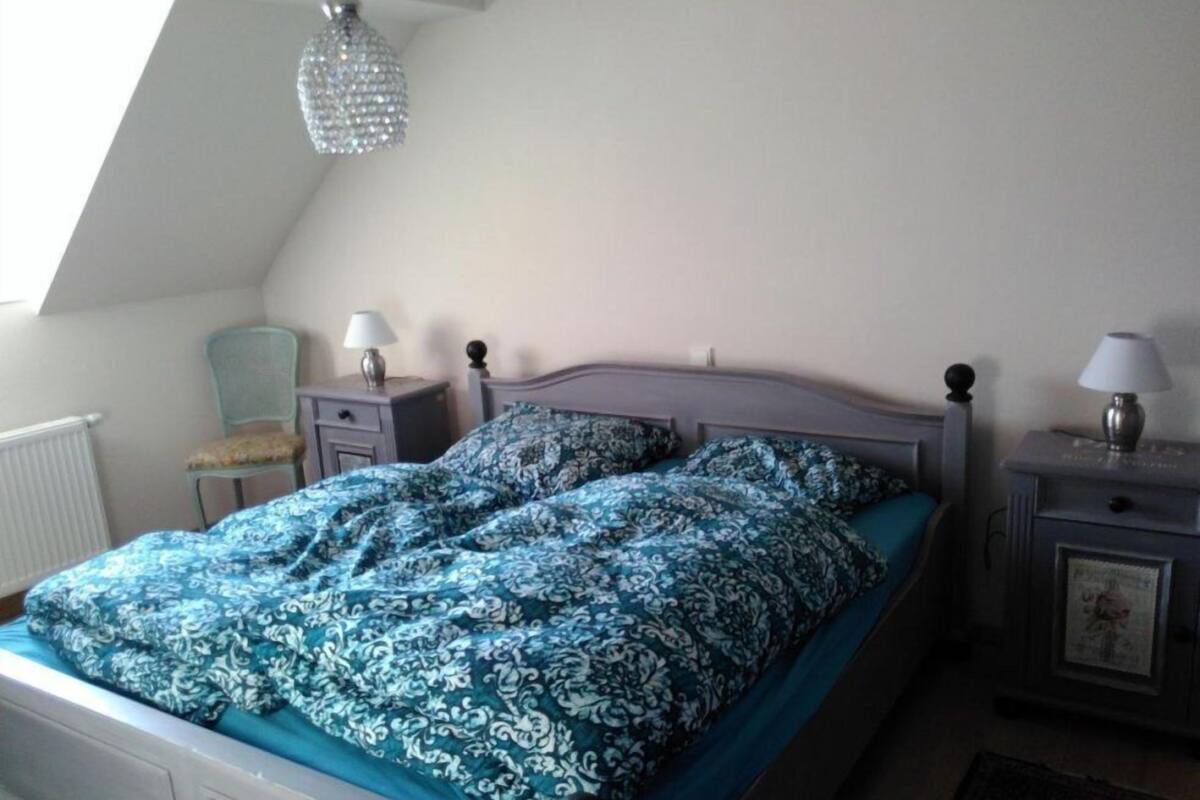 Een slaapkamer met een bed, twee nachtkastjes, een stoel, een radiator en een kroonluchter.