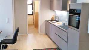 A modern kitchen with light wood flooring, a colorful rug, and a view into the dining area.