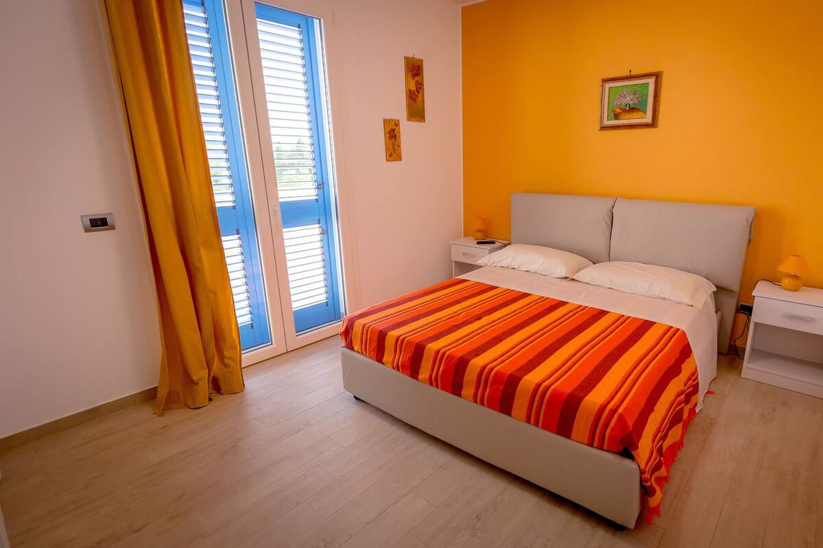 Une chambre à coucher avec un lit, une table de chevet, une lampe et une fenêtre avec des rideaux.