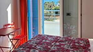 Een slaapkamer met een bed, een stoel, een raam met uitzicht op zee en een deur naar een buitenbalkon.