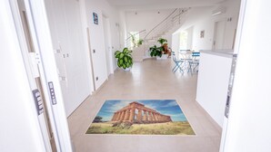 Een hal met een groot muurschildering van een oud gebouw op de vloer, die leidt naar een trap en een eetruimte met stoelen en tafels.