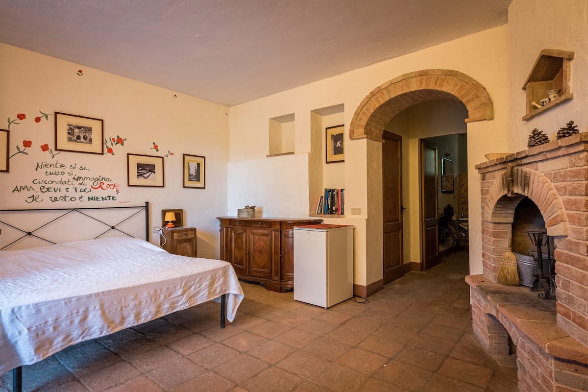 Ein Schlafzimmer mit Bett, Kommode, einem kleinen Tisch, Kamin und einem Flur, der zu einem anderen Raum führt.