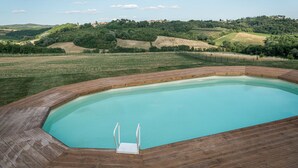 Une piscine dotée d’une terrasse en bois, entourée d’un paysage vallonné.