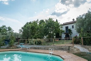 Relax by the serene pool surrounded by lush greenery and a traditional building.