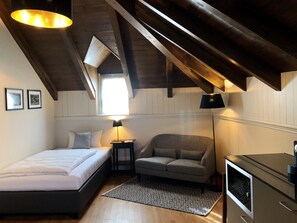 A bedroom with a bed, a grey sofa, a small table with a lamp, and a TV. - Marco Polo Business Apartments Sonne - Bremgarten (Bremgarten)