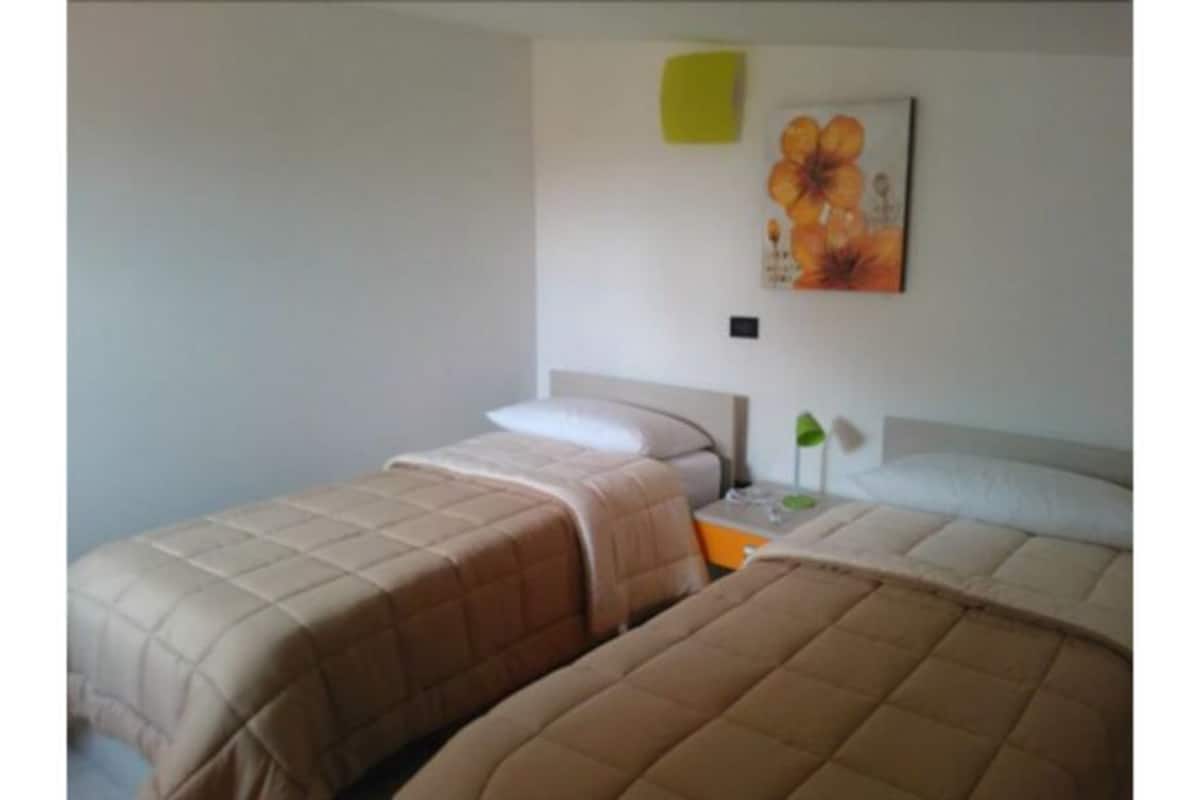 A room with two beds, a nightstand, a lamp, and a painting on the wall.