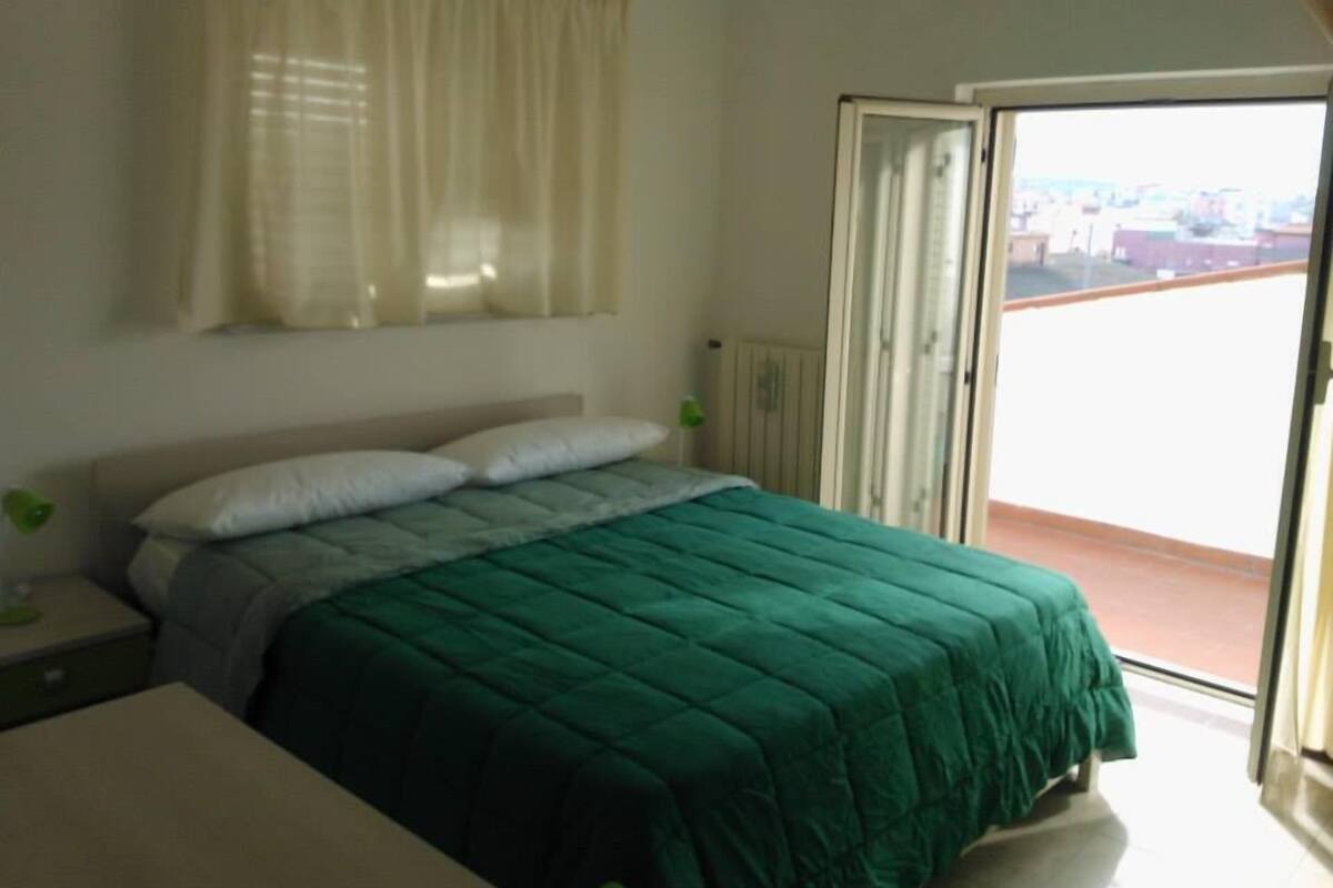 A bedroom with a bed, a nightstand, a window with curtains, and a sliding glass door to an outdoor area.