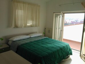 A bedroom with a bed, a nightstand, a window with curtains, and a sliding glass door to an outdoor area.