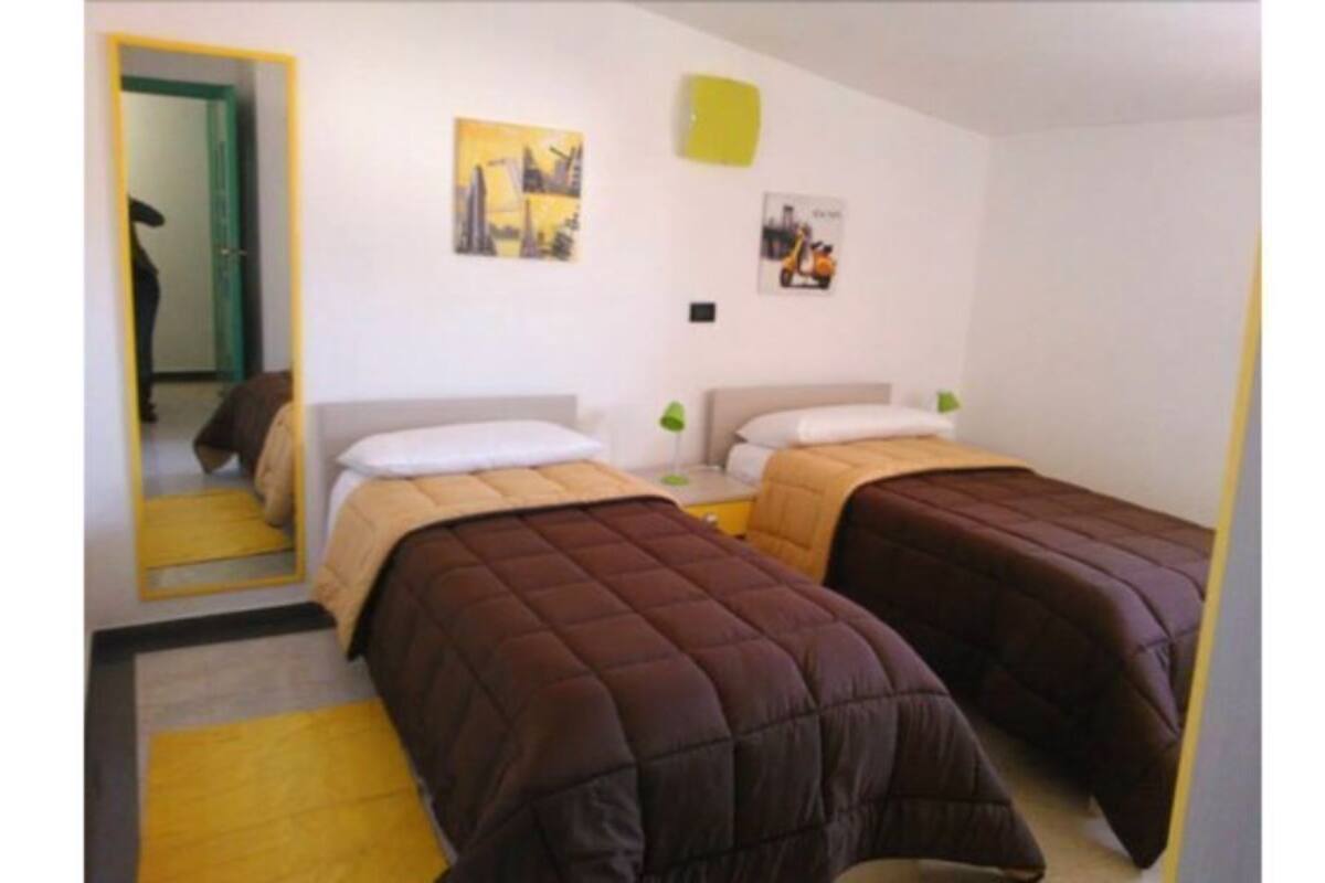 A room with two beds, a mirror, and a door leading to another room.