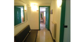 Un pasillo estrecho con un banco a la izquierda, una puerta al final y un marco de puerta verde a la derecha.